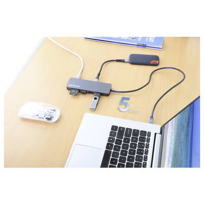 Ein Laptop ist über einen mit '5 Gbps' beschrifteten USB-Hub mit mehreren Geräten verbunden. In der Nähe befinden sich ein Buch, eine weiße Maus und eine externe Festplatte.