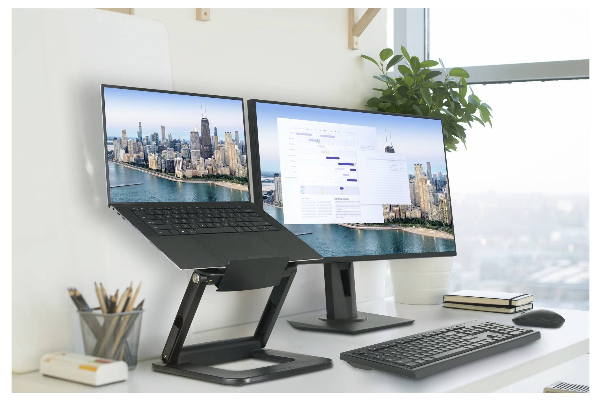 Ein moderner Arbeitsplatz mit einem Laptop auf einem Ständer und zwei Monitoren, die eine Stadtlandschaft und einen Projektablaufplan zeigen. Eine Pflanze steht in der Nähe.