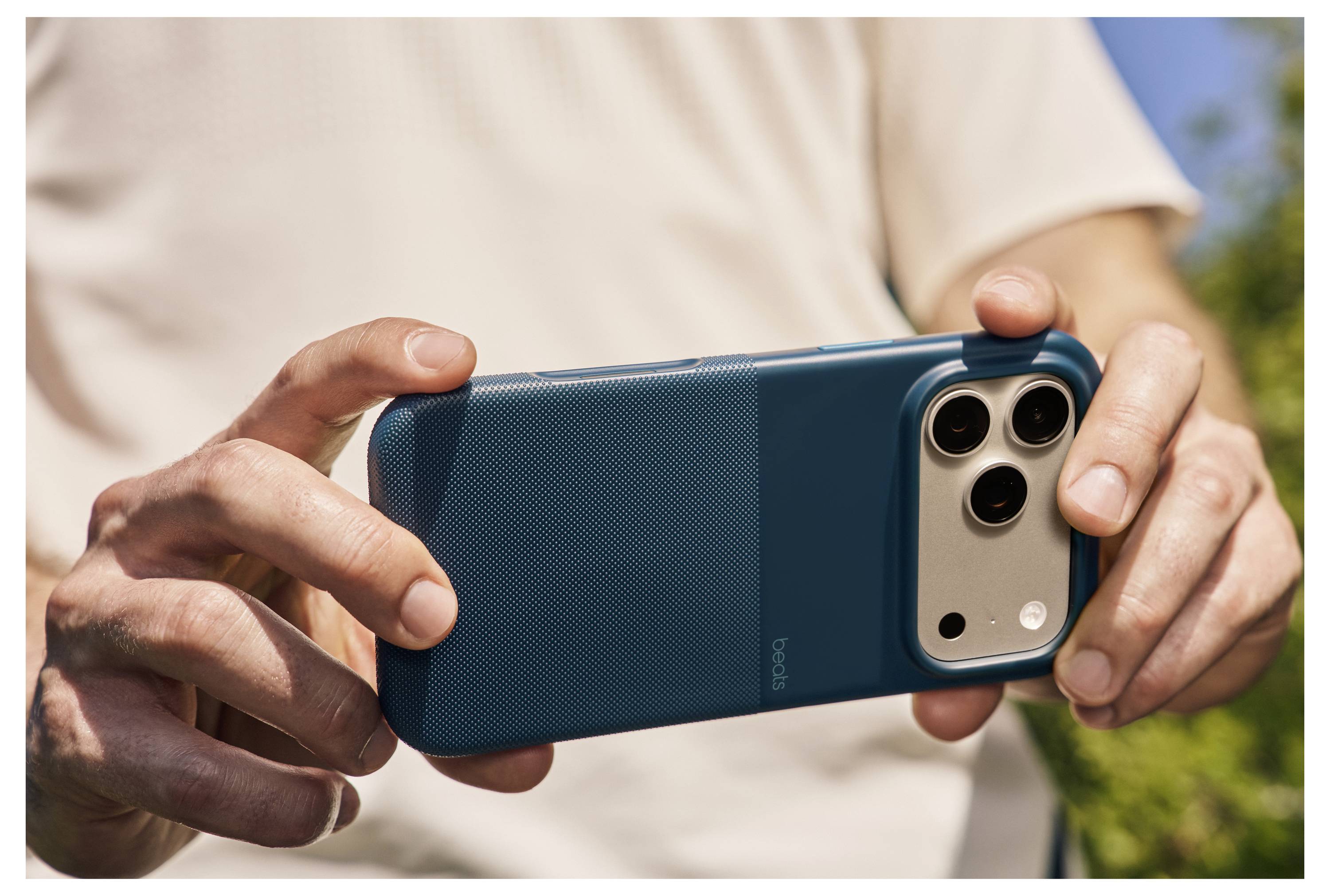 Eine Person in einem weißen Hemd hält ein Smartphone horizontal und macht ein Foto vor einem unscharfen Hintergrund im Freien.