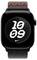 Eine Smartwatch mit einem schwarzen Bildschirm zeigt die Uhrzeit '10:09' in großen weißen Zahlen über einem geometrischen Hintergrundmuster. Die Uhr hat ein schwarzes Gehäuse und ein graues Armband mit rotem Akzent.