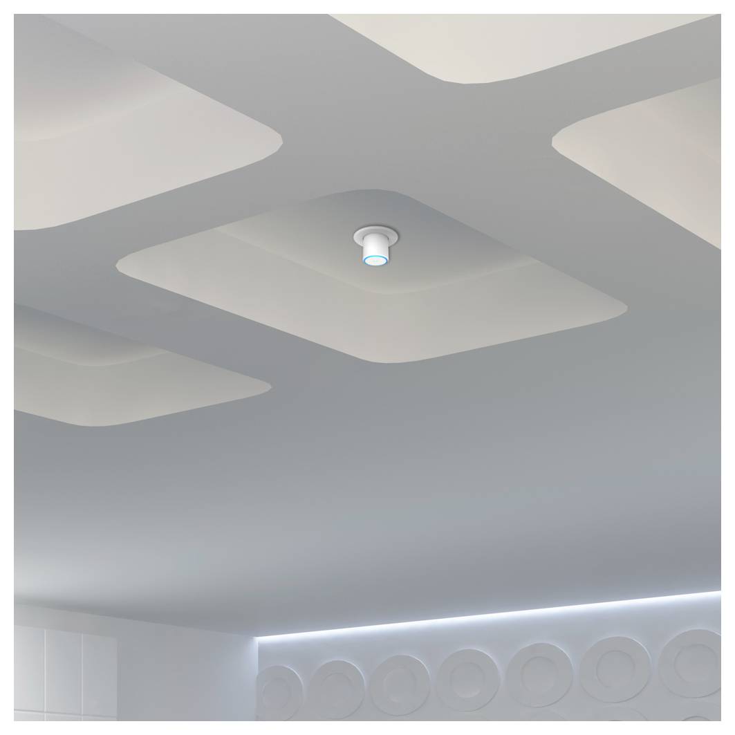 Eine moderne Decke mit einem kleinen runden Rauchmelder, der in einem dämmrig beleuchteten Raum ein weiches grünes Licht ausstrahlt.