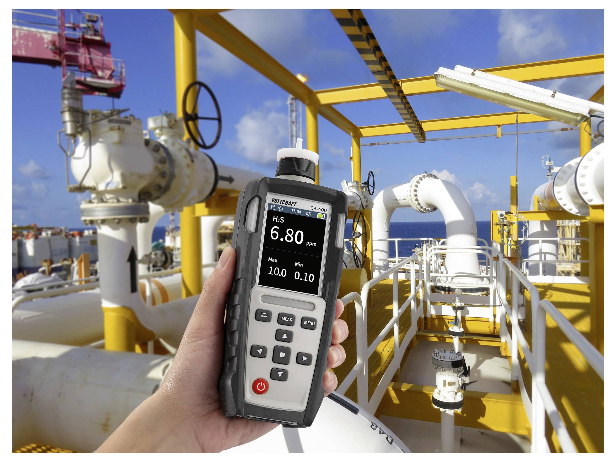 Hand hält ein Gasdetektor, das "H2S 6,80 PPM" auf einer gelben Industriepipeline-Plattform unter blauem Himmel zeigt.