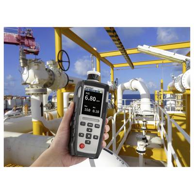 Hand hält ein Gasdetektor, das "H2S 6,80 PPM" auf einer gelben Industriepipeline-Plattform unter blauem Himmel zeigt.