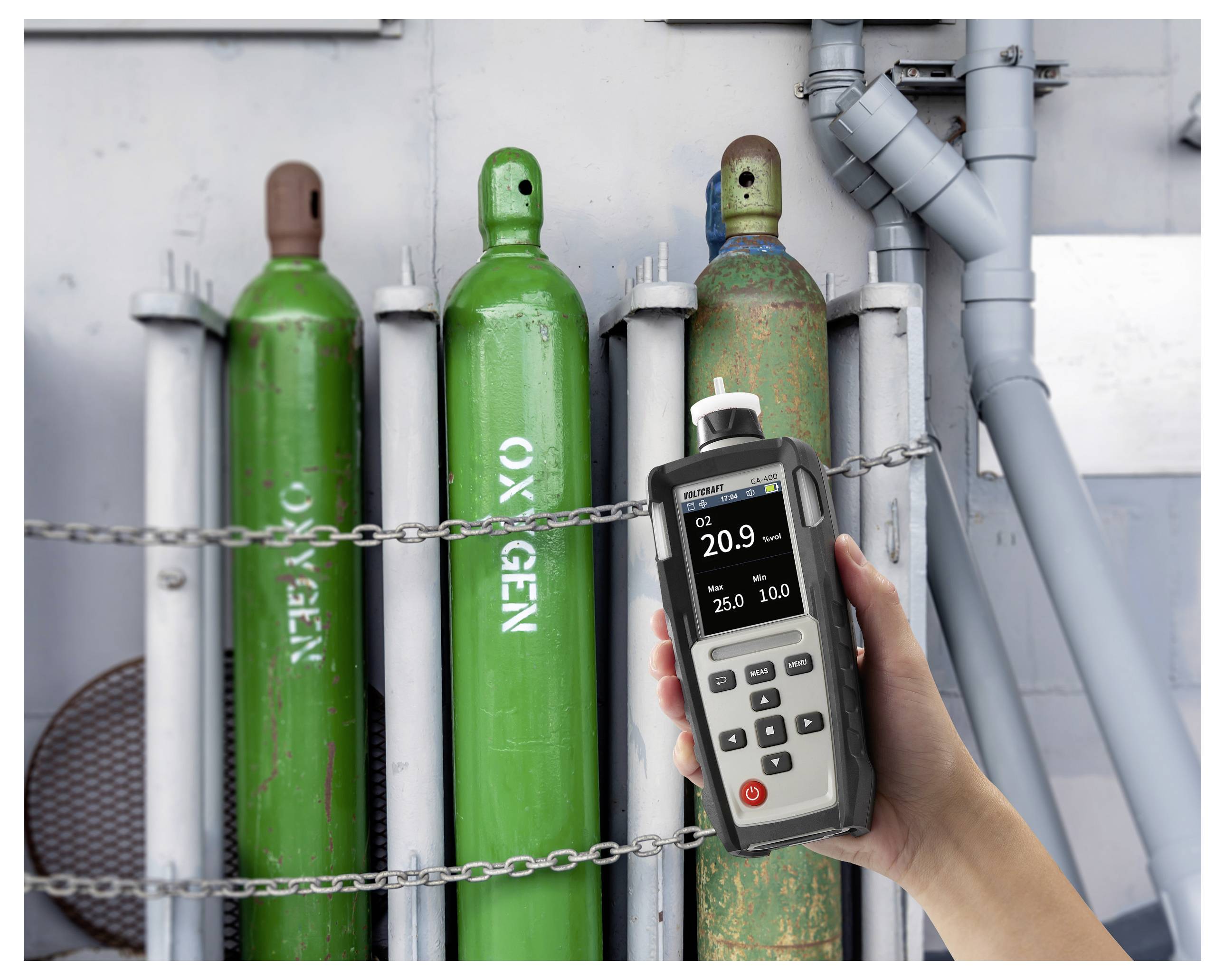Eine Hand hält ein Gasprüfgerät mit einer Anzeige von „20,9" in der Nähe von geketteten grünen Sauerstofftanks, was auf einen sicheren Sauerstoffgehalt hinweist.