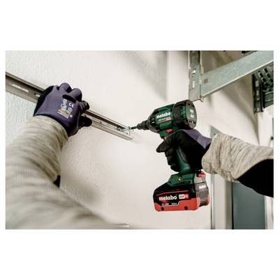 Eine Person verwendet eine grün-rote Bohrmaschine, um eine Metallhalterung an einer weißen Wand zu befestigen und trägt dabei Handschuhe zum Schutz.