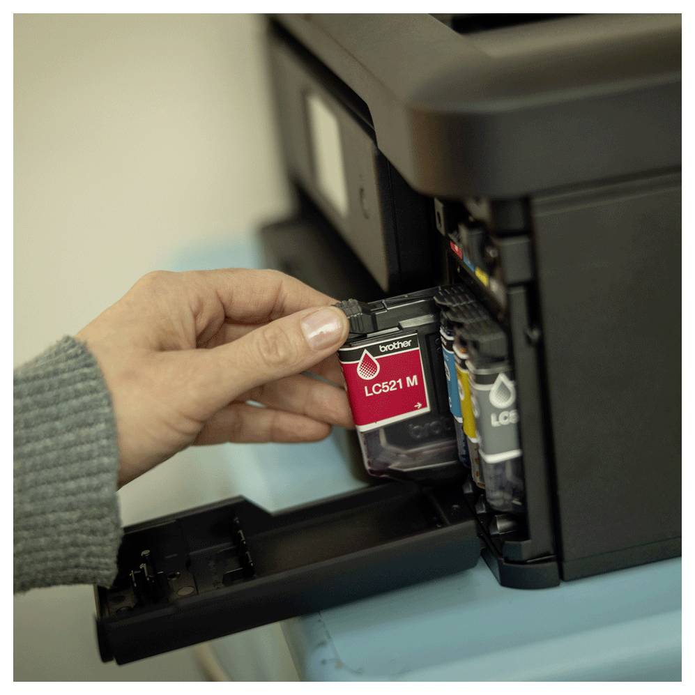 Eine Hand bringt eine rote Tintenpatrone mit der Bezeichnung "LC521 M" in einen Drucker ein, was auf Wartung oder Einrichtung des Druckertintensystems hindeutet.