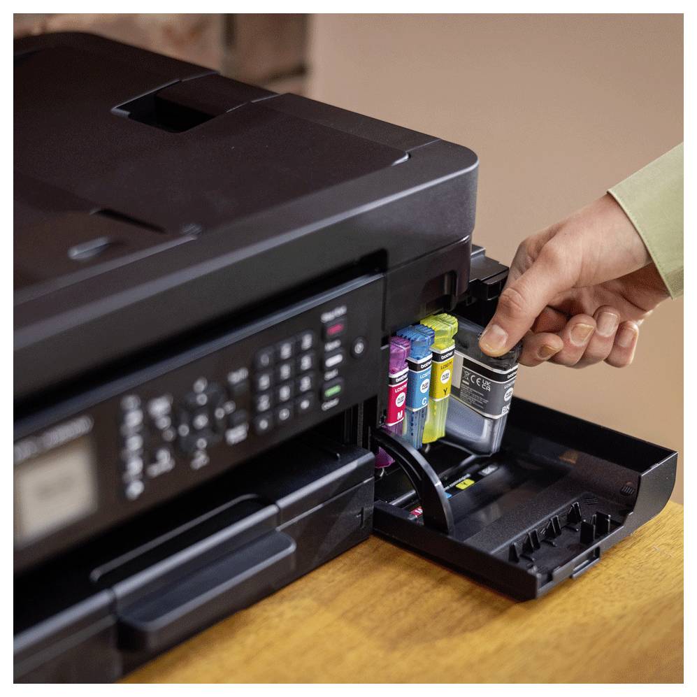 Eine Person ersetzt eine schwarze Tintenpatrone in einem Farbdrucker, wobei die Magenta-, Gelb- und Cyan-Patronen sichtbar sind.