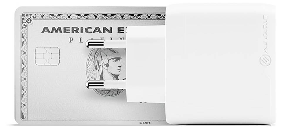 Ein weißer Netzteiladapter verdeckt teilweise eine Graustufen-Karte mit dem Text "American Express Platinum" und einer klassischen Figur.