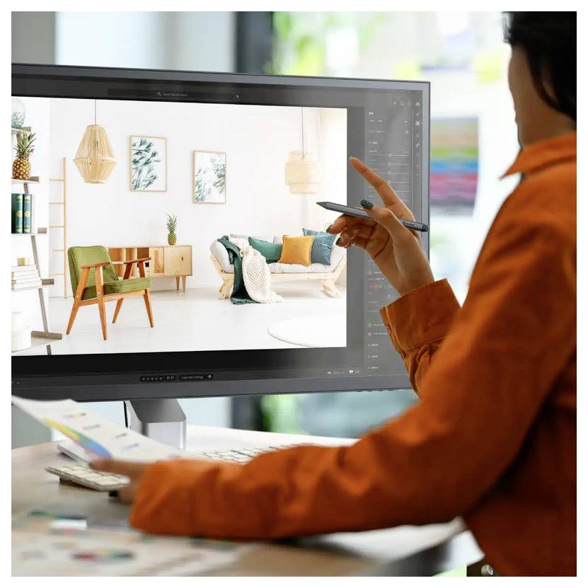 Eine Person in einem orangefarbenen Shirt verwendet einen Stylus auf einem Tablet, um ein modernes Wohnzimmer-Interieur zu gestalten, das auf einem großen Computerbildschirm sichtbar ist.