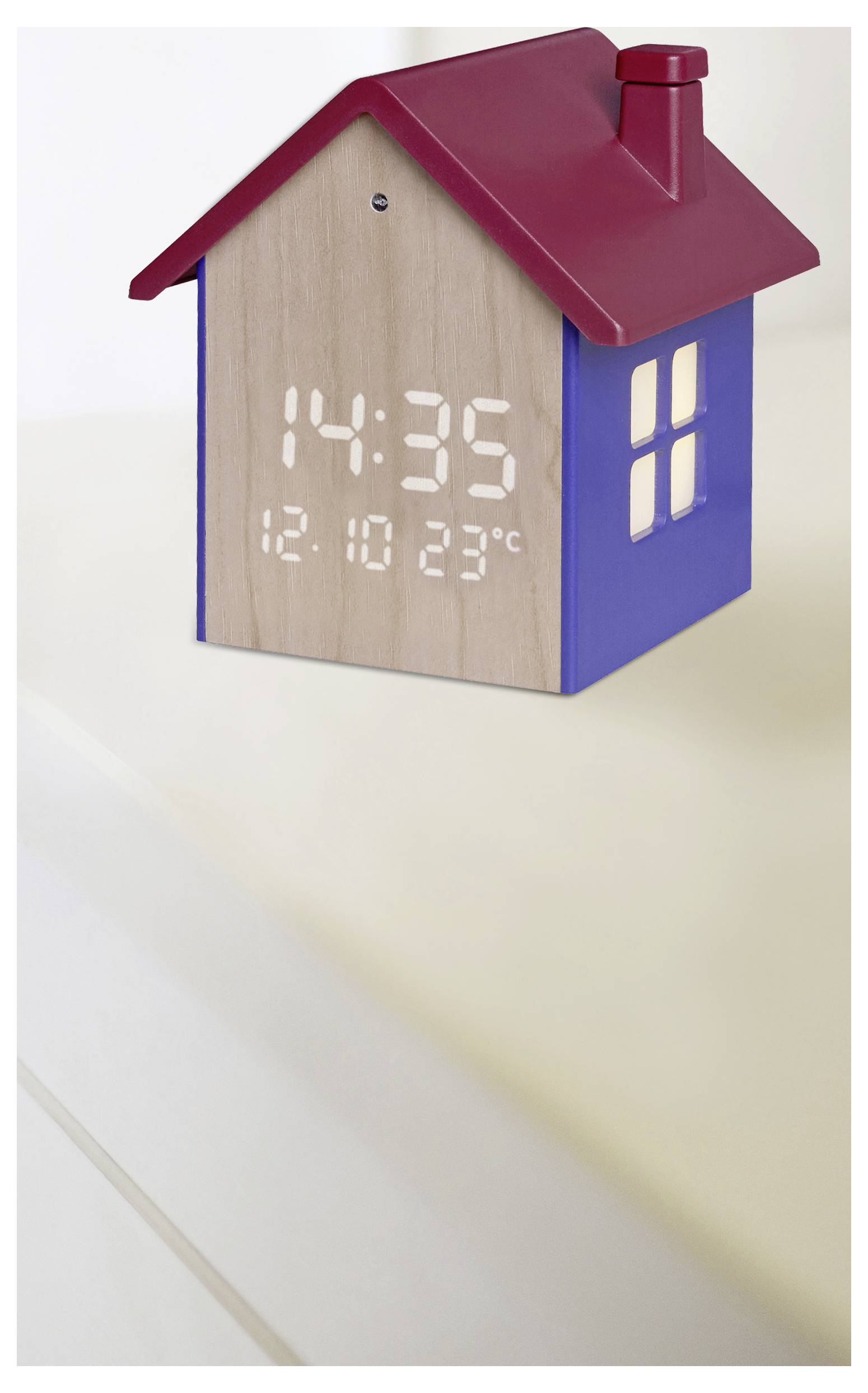 Eine hausförmige Uhr mit einer holzmaserungstexturierten Vorderseite zeigt die Zeit '14:35', das Datum '12.10' und die Temperatur '23°C'. Sie hat ein rotes Dach und blaue Wände.