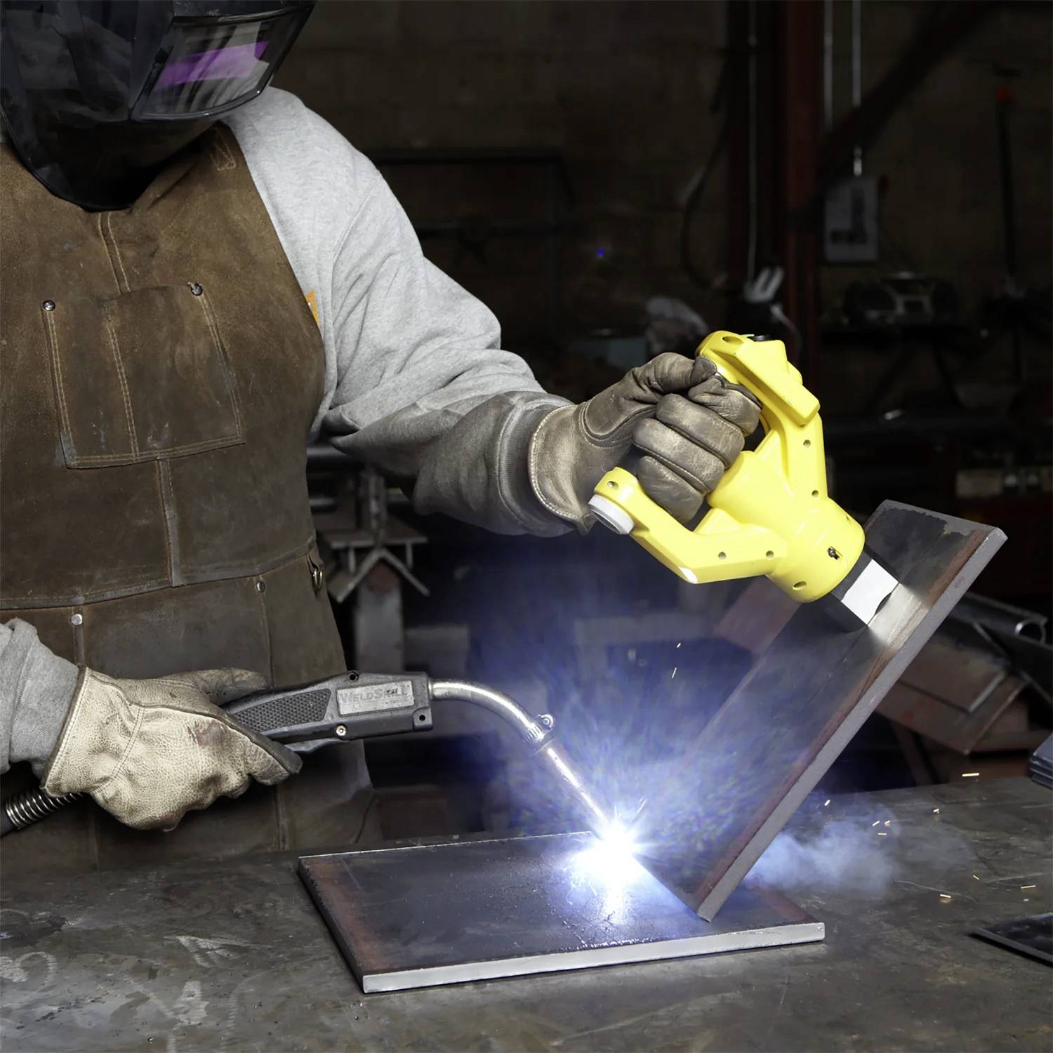 Ein Schweißer mit Schutzausrüstung verwendet einen Schweißbrenner an Metallteilen und erzeugt helle Funken in einer Werkstattumgebung.