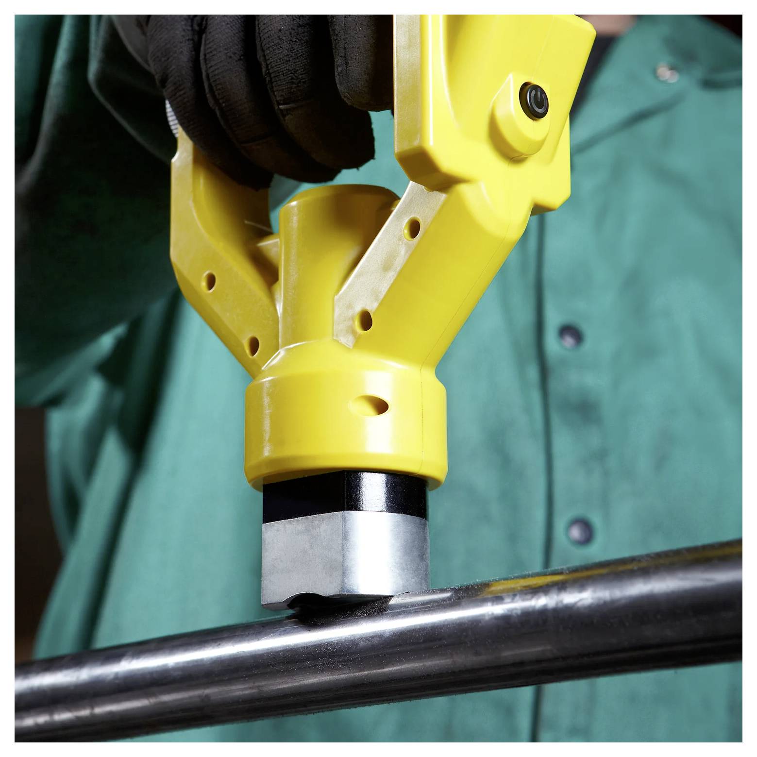 Ein Arbeiter in grüner Uniform verwendet eine gelbe Magnetbohrmaschine, um ein Metallrohr zu befestigen und industrielle Ausrüstung in Aktion zu demonstrieren.