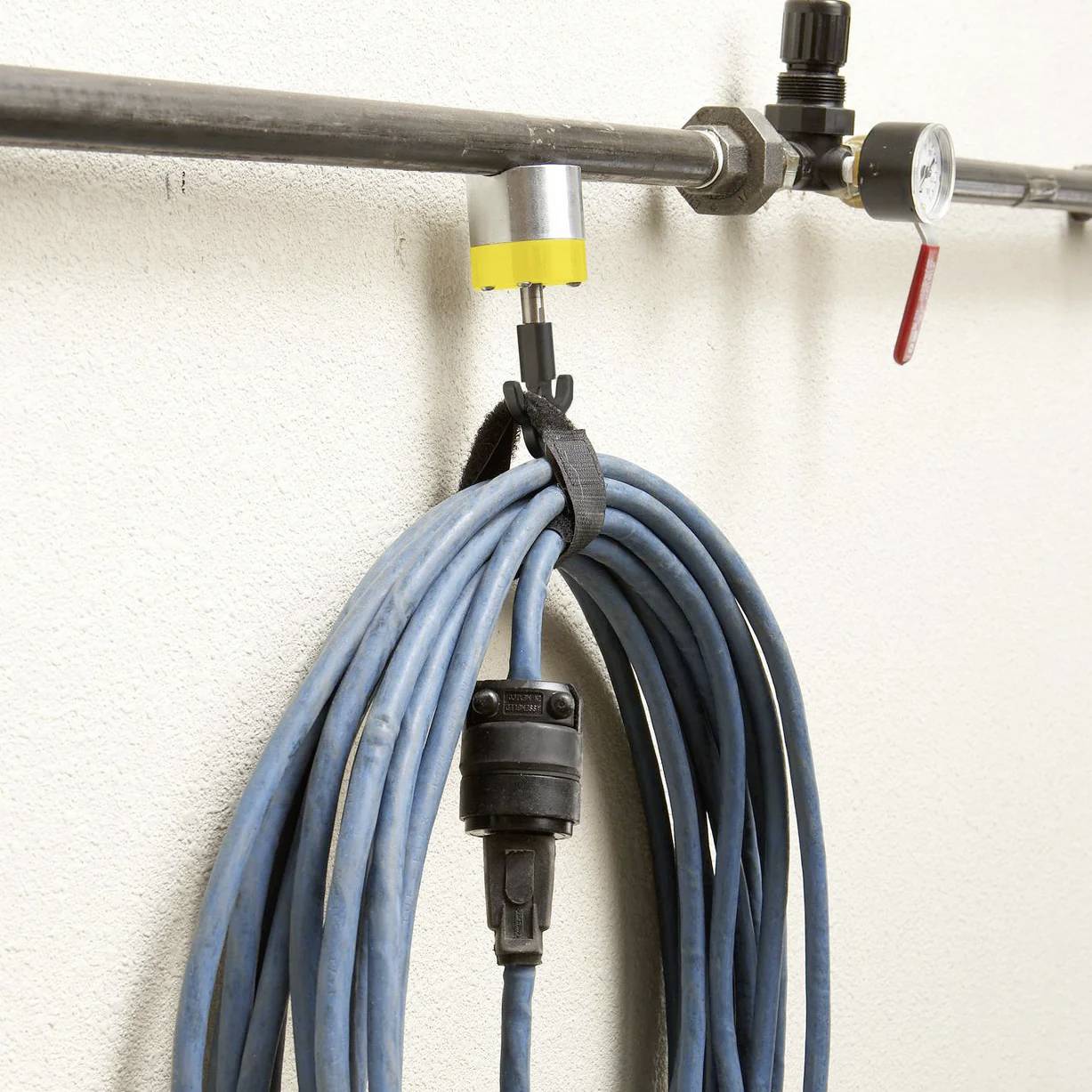 Ein blauer Schlauch, aufgerollt und an einem wandmontierten Haken hängend, unter einem Rohr mit einem Manometer und einem Ventil.