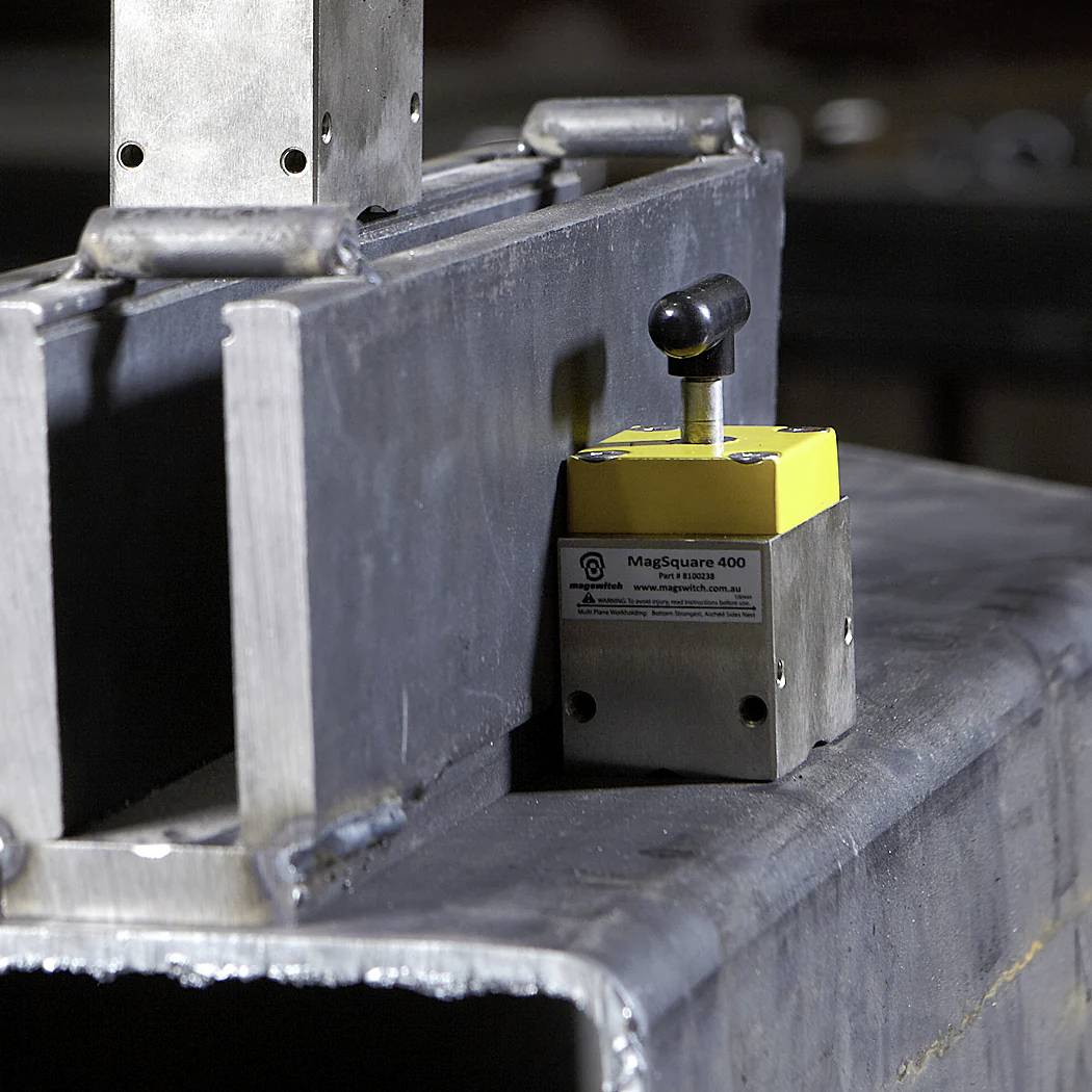 Eine gelbe MagSquare 400 Metallklemme hält Stahlträger zusammen und deutet auf industrielle Montage oder Bauarbeiten hin.