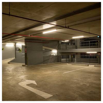 Leerer Indoor-Parkgarage mit markierten Parkplätzen, Deckenbeleuchtung und einem Richtungspfeil auf dem Boden, der eine Linkskurve anzeigt.