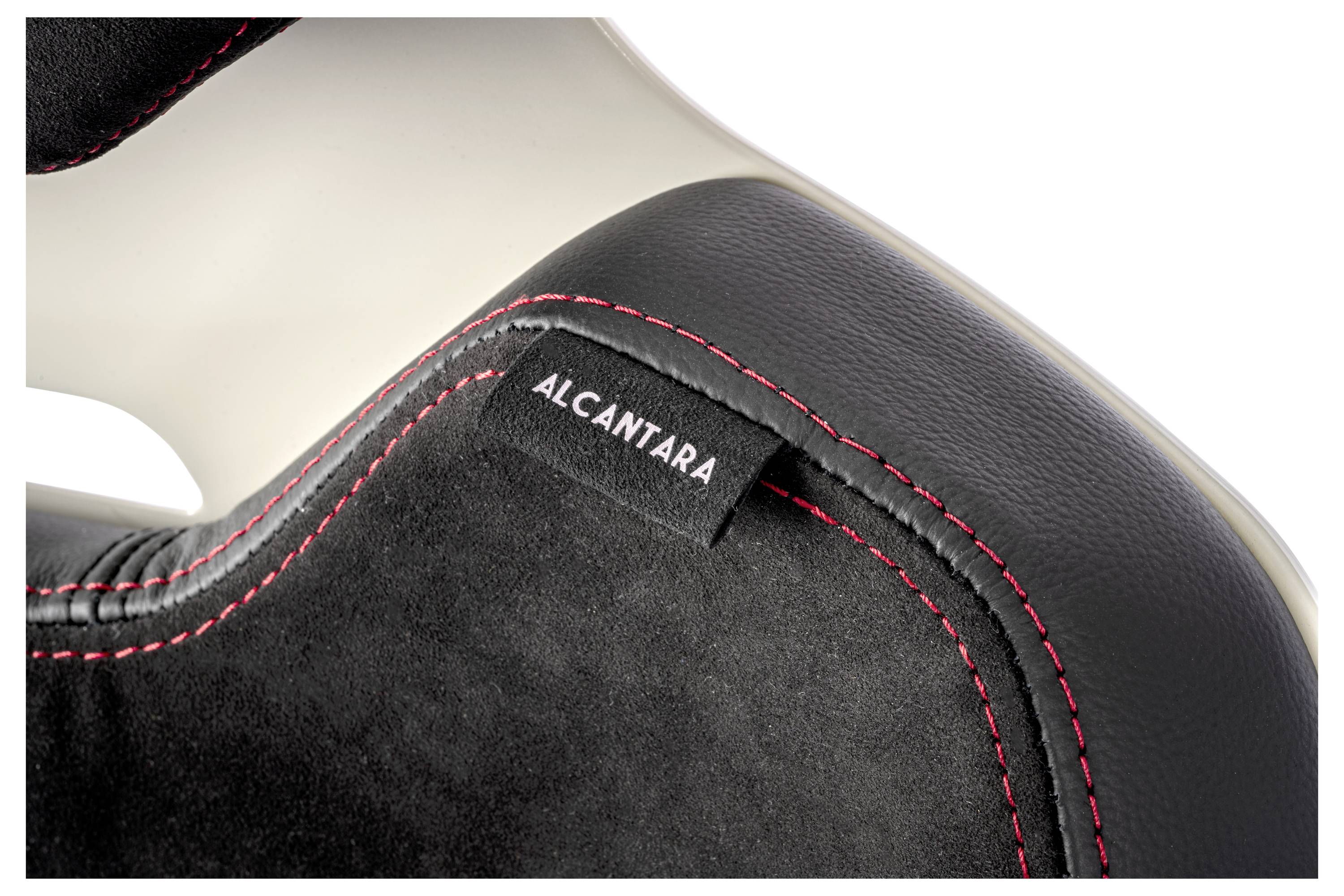 Nahaufnahme eines Autositzes mit schwarzem Alcantara-Stoff, roter Ziersteppung und einem Alcantara-Markenetikett, was Luxus und Handwerkskunst betont.