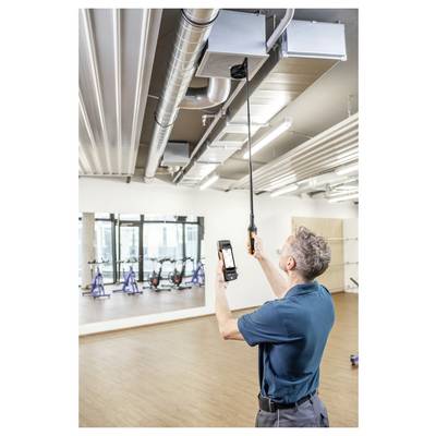 Eine Person in einem blauen Hemd inspiziert Lüftungskanäle in einem Fitnessstudio und verwendet dabei ein Handgerät und ein Smartphone zur Messung.