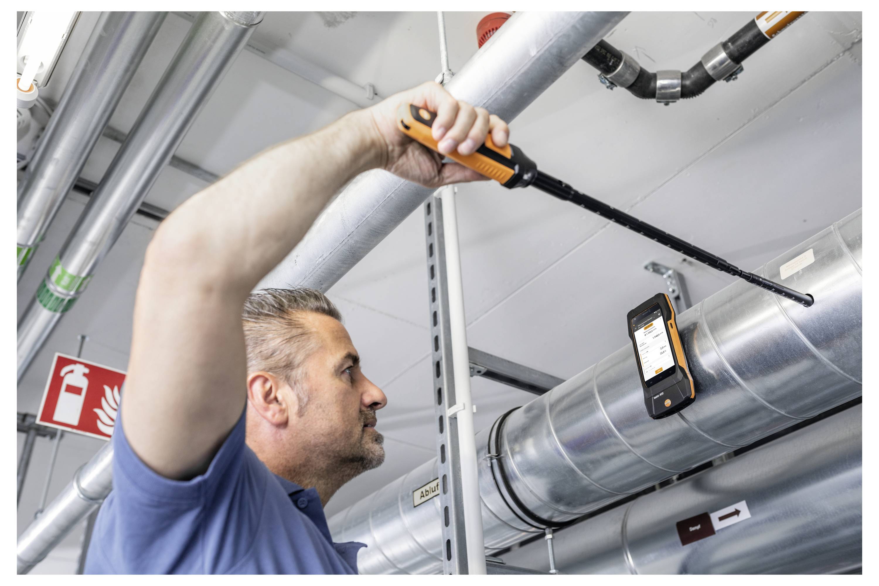 Eine Person, die ein tragbares Gerät verwendet, um Luftkanäle in einem industriellen Umfeld zu überprüfen, möglicherweise zur Durchführung von Wartungs- oder Inspektionsarbeiten.