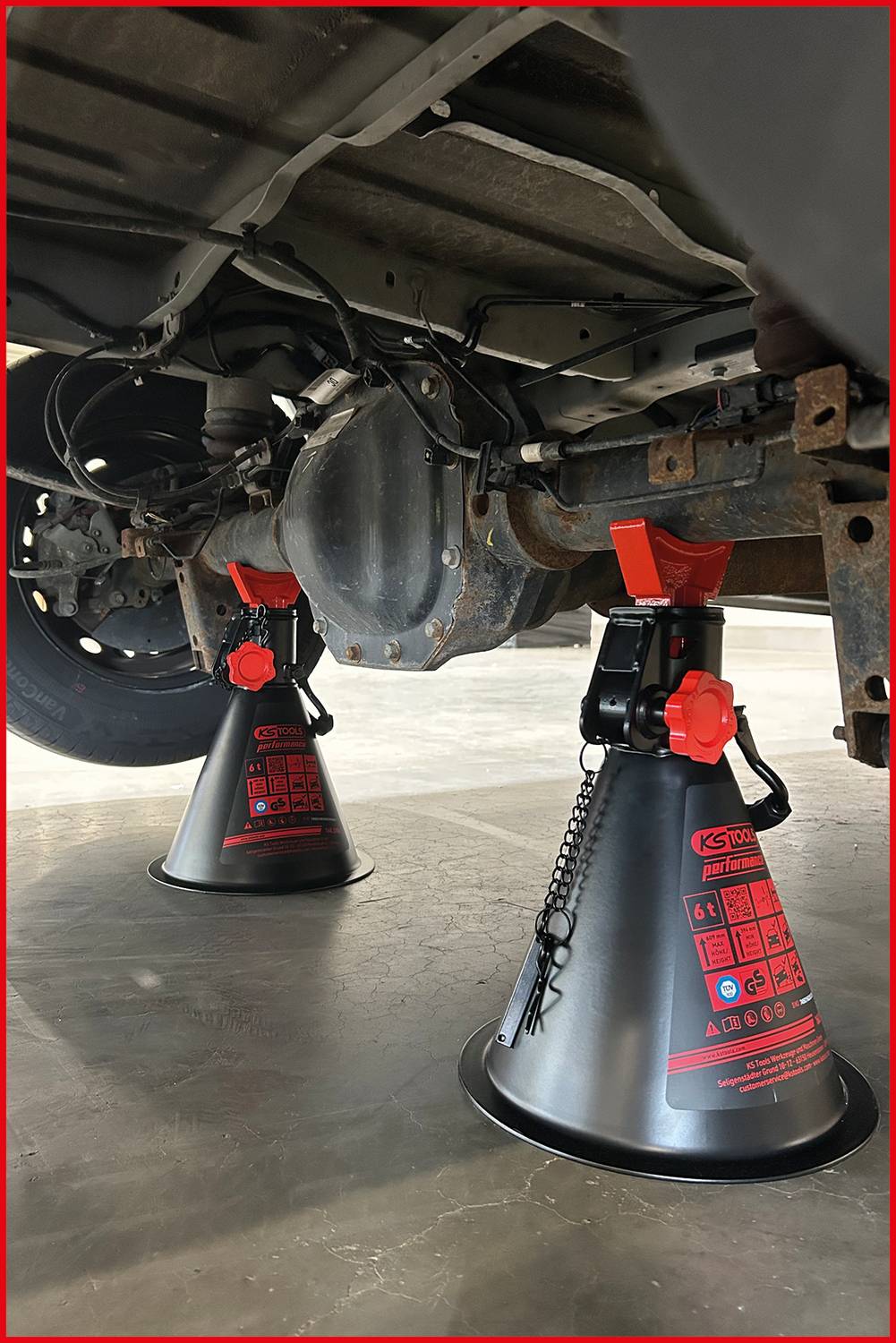 Zwei Wagenheber stützen die Hinterachse eines Fahrzeugs in einer Garage, was auf Wartungs- oder Reparaturarbeiten an der Fahrzeugunterkante hinweist.
