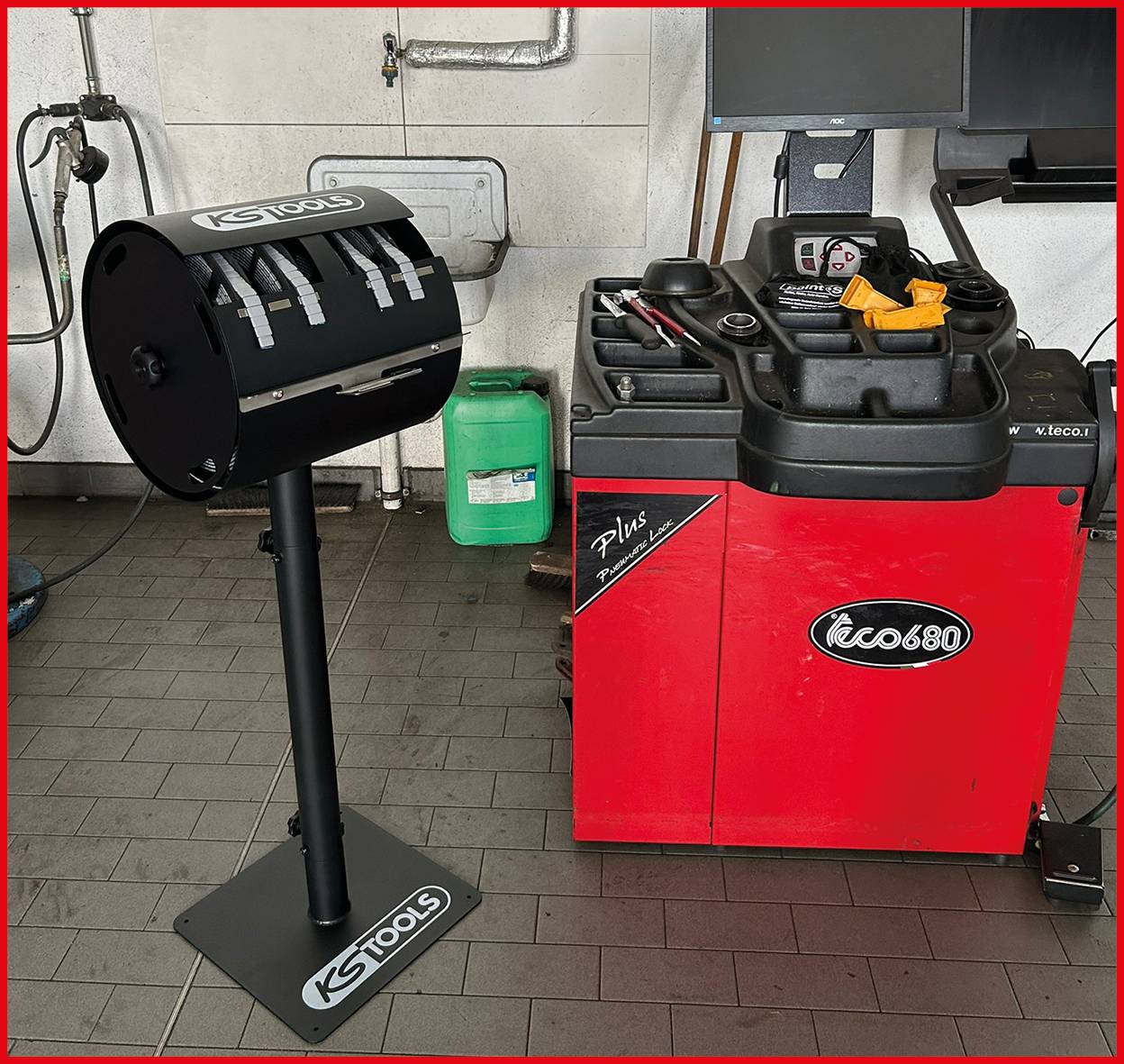 Eine KS Tools Reifenauswuchtmaschine steht in einer Werkstatt mit darauf angeordneten Werkzeugen. Ein Behälter mit Flüssigkeit befindet sich in der Nähe, vor einer gefliesten Wand.