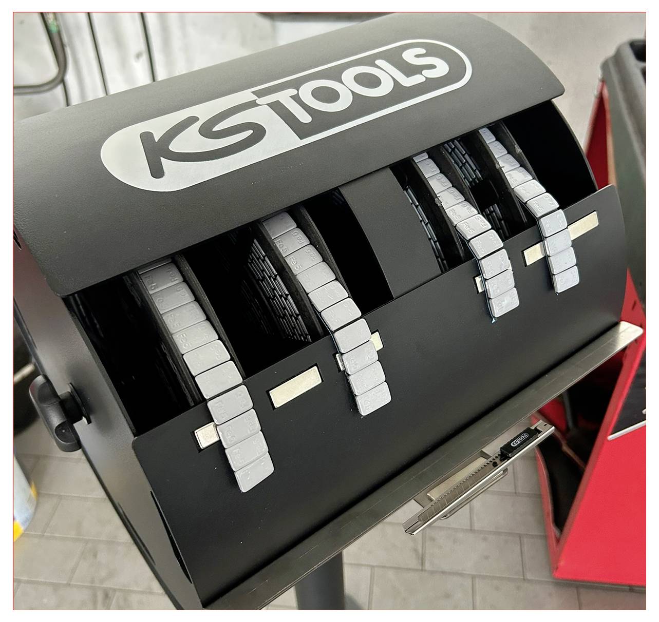 Ein Ausgabegerät mit mehreren Reihen grauer Metallgewichte, die mit "KS TOOLS" für die Reifenauswuchtung beschriftet sind.