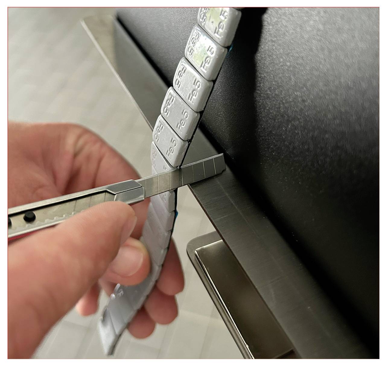 Eine Hand schneidet einen metallischen Streifen mit Zahlen mithilfe eines Universalmessers und passt wahrscheinlich ein anpassbares Element an.