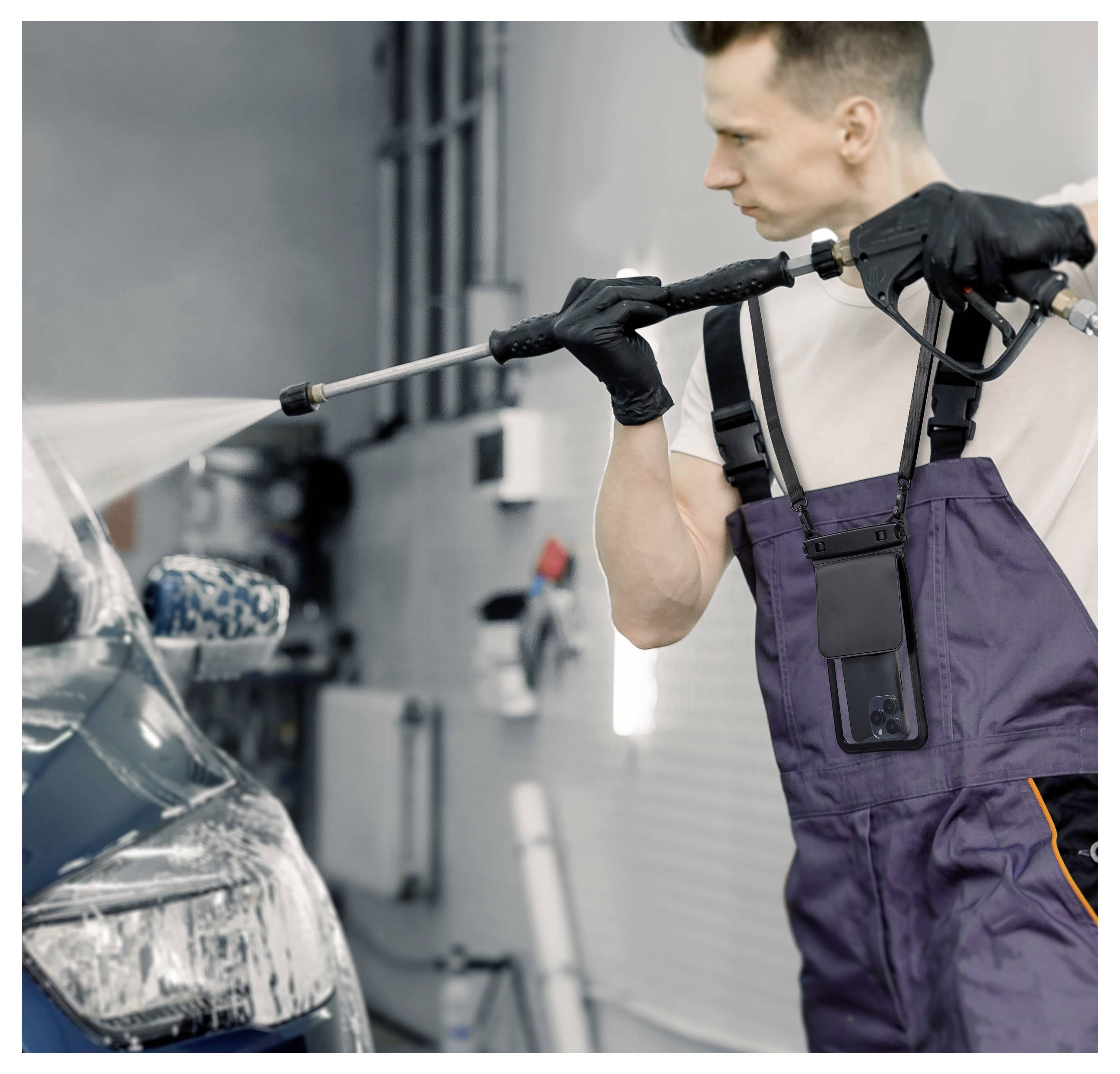 Ein Arbeiter in Arbeitskleidung reinigt einen blauen Wagen mit einem Hochdruckreiniger in einer Garage, wobei er sich auf den vorderen Scheinwerfer konzentriert, schwarze Handschuhe trägt und einen Schlauch benutzt.