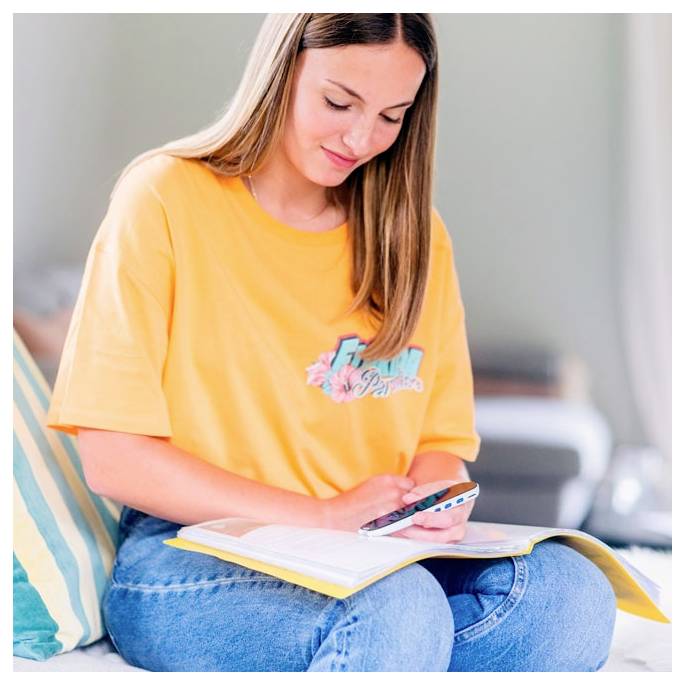 Eine Person in einem gelben Hemd sitzt entspannt auf einem Sofa, lächelt und schreibt mit einem Stift in ein Notizbuch. Die Atmosphäre ist locker und ungezwungen.