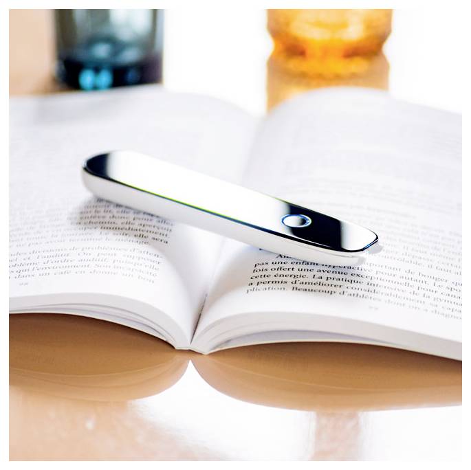 Ein schlankes silbernes Gerät liegt über einer Buchseite, was auf seine Verwendung zur Leseunterstützung in entspannter Umgebung hindeutet.