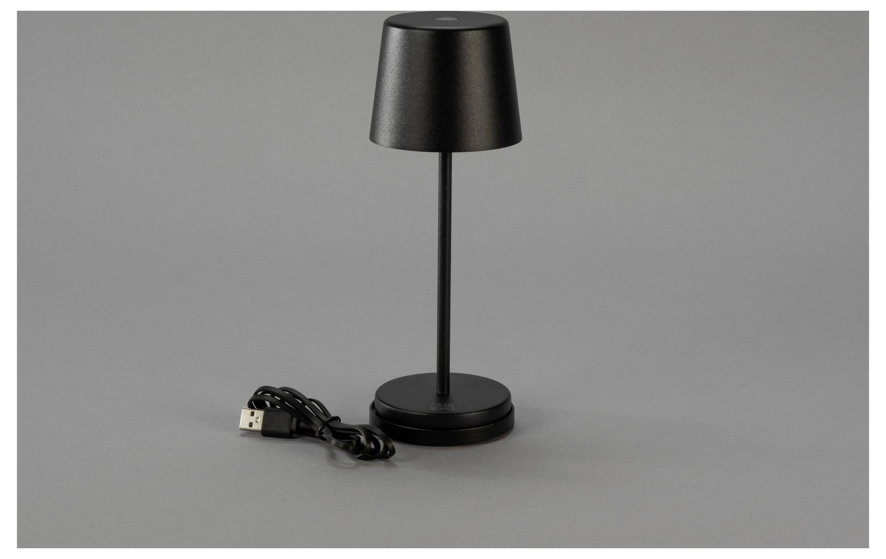 Eine schlanke, moderne schwarze Tischlampe mit einem USB-Kabel daneben auf einem grauen Hintergrund. Die Lampe hat einen konischen Lampenschirm und eine runde Basis.