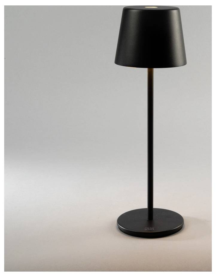 Eine schwarze, moderne Tischlampe mit schlankem Ständer und kegelförmigem Lampenschirm steht auf einer ebenen Oberfläche und wirft ein weiches Licht auf den Bereich darunter.