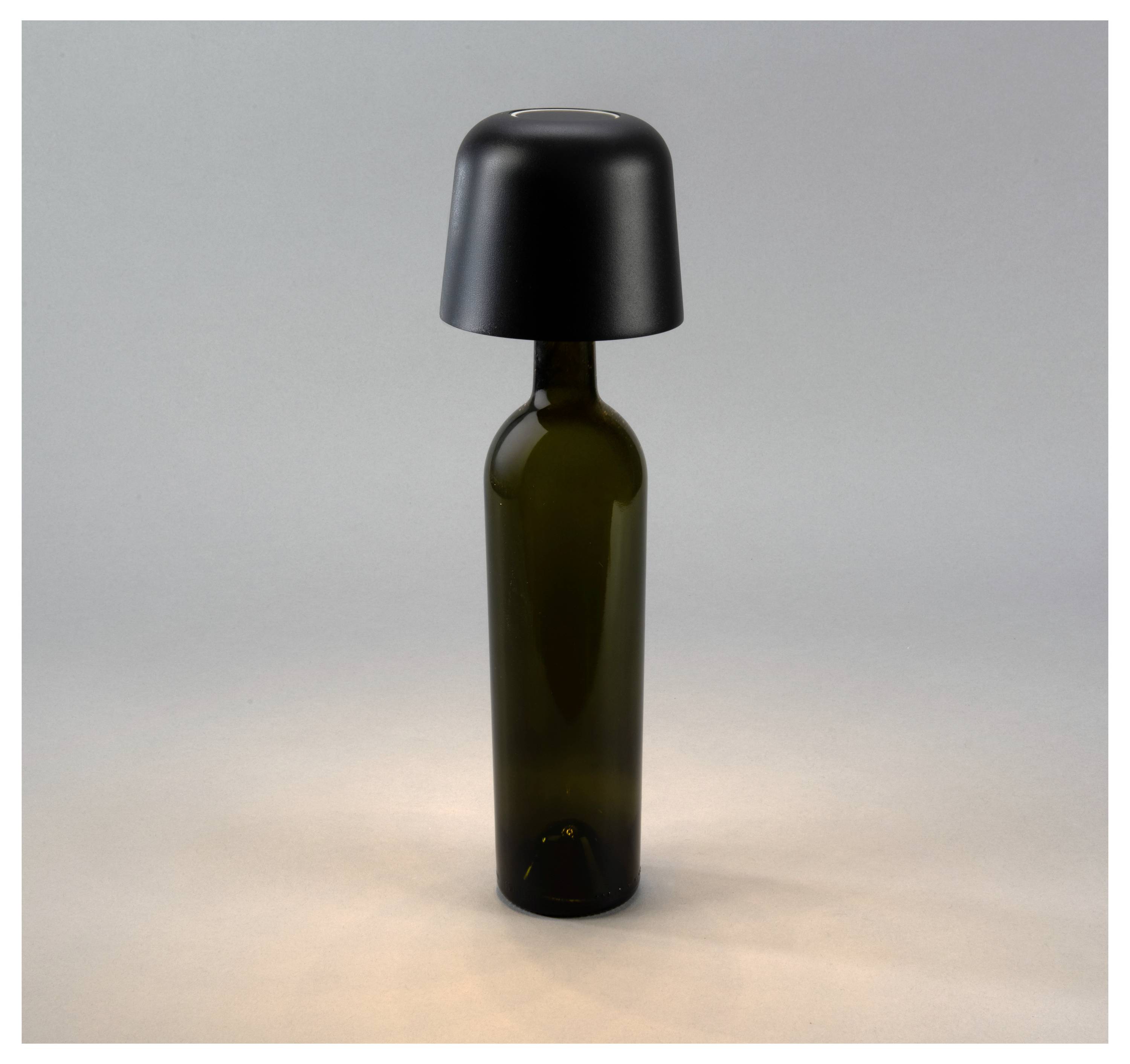 Eine dunkelgrüne Weinflasche mit einem schwarzen Lampenschirm obenauf, die einer Lampe ähnelt, vor einem neutralen Hintergrund.