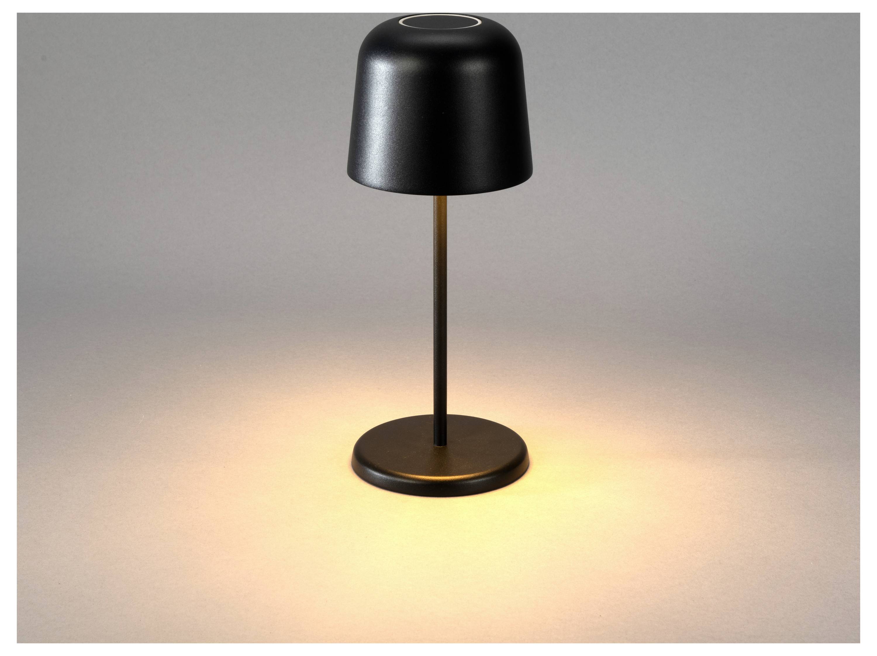 Eine schwarze Tischlampe verbreitet ein warmes Leuchten auf einer grauen Oberfläche und erzeugt eine gemütliche Atmosphäre.