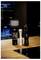Eine Flasche mit einer kleinen Lampe daran steht auf einer Holztheke, neben weißen und schwarzen Pfeffermühlen. Der Hintergrund ist sanft beleuchtet.