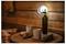Eine rustikale Tischdecke mit zwei Bechern, Servietten und einer braunen Flasche, die eine brennende Lampe trägt, vor einer Holzwand, die eine gemütliche Atmosphäre schafft.