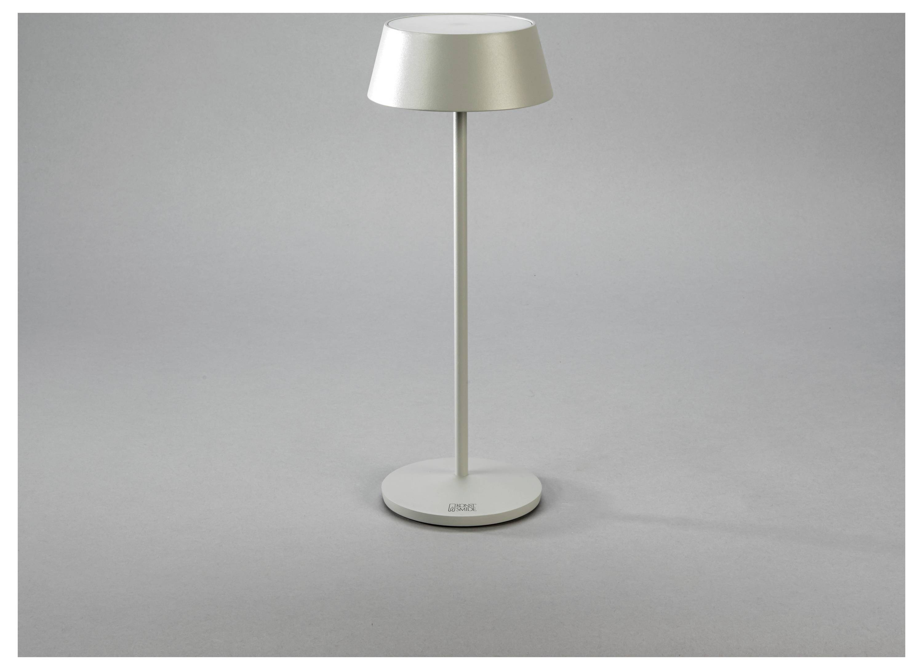 Eine moderne, minimalistische silberne Tischlampe mit rundem Fuß und Schirm, die vor einem neutralen Hintergrund steht.