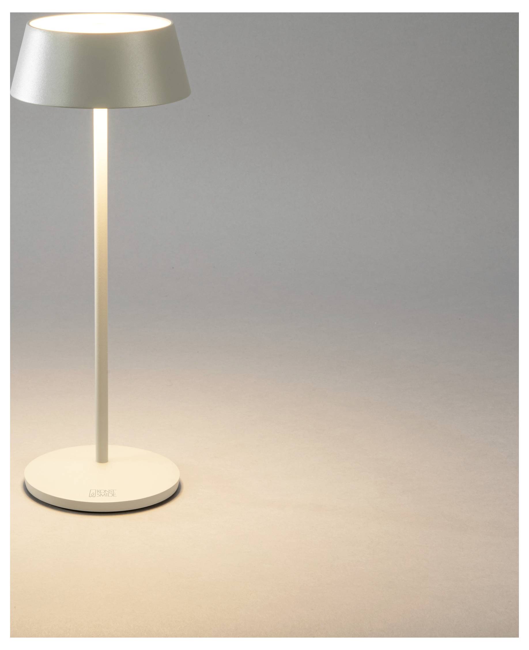 Eine schlanke, moderne Tischlampe mit glatter Metalloberfläche, die warmes Licht auf einen neutralen Hintergrund wirft.