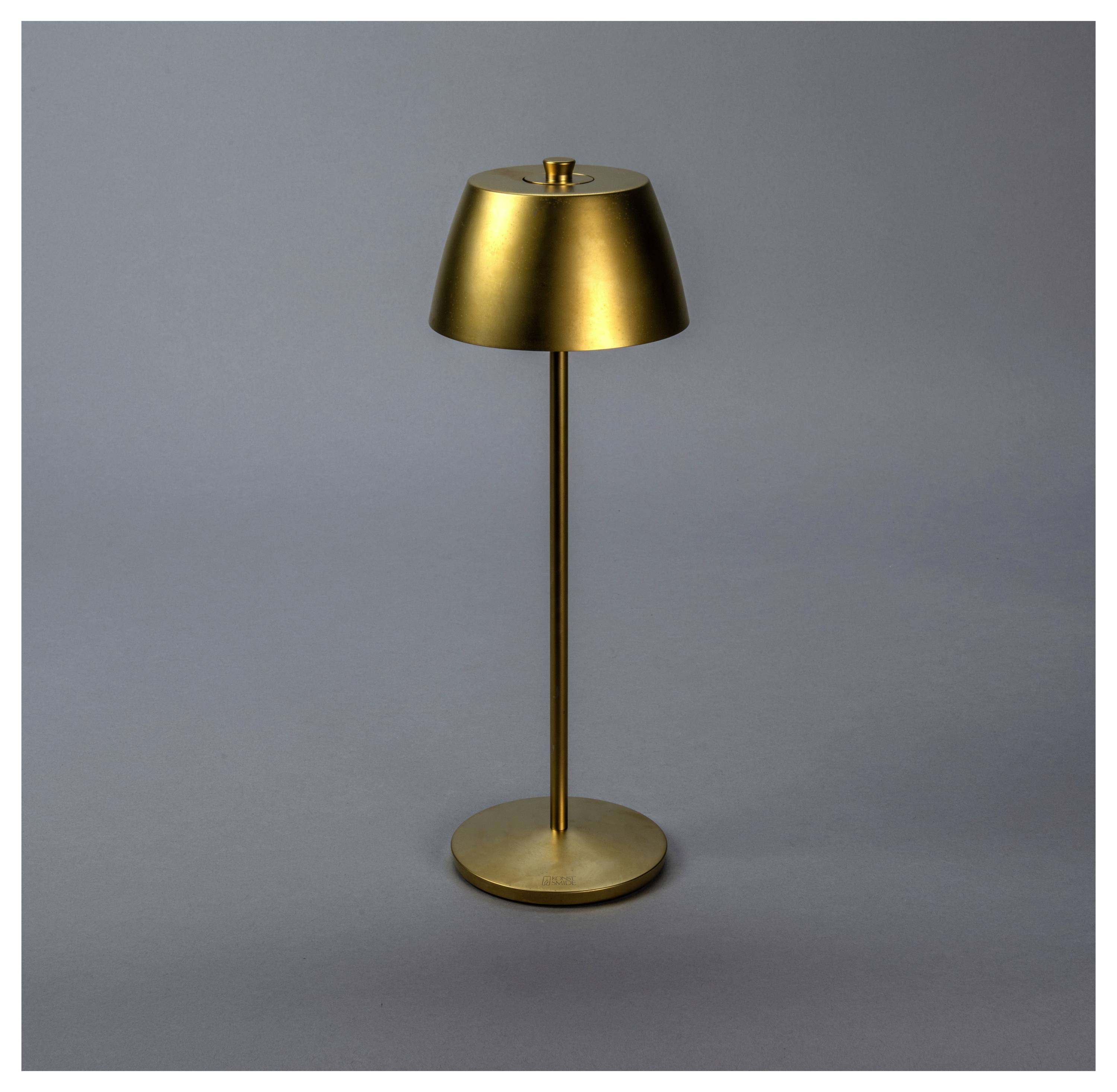 Eine elegante, moderne Messinglampe mit einer zylindrischen Basis und einem breiten, konischen Schirm, vor einem schlichten grauen Hintergrund.