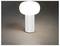 Eine moderne Tischlampe mit einer zylindrischen Basis und einem ovalen, leuchtenden Oberteil strahlt weiches weißes Licht auf einer dunklen Oberfläche aus.