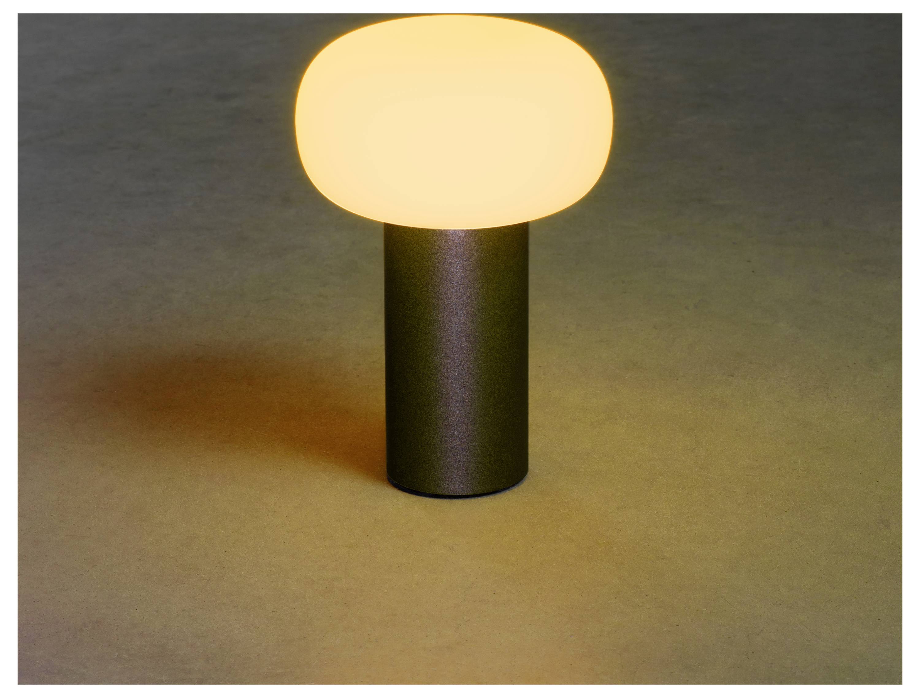 Eine kleine, moderne Tischlampe mit weichem, gelblich schimmerndem Licht auf einer dunklen zylindrischen Basis, die einen sanften Schein auf die Oberfläche wirft.