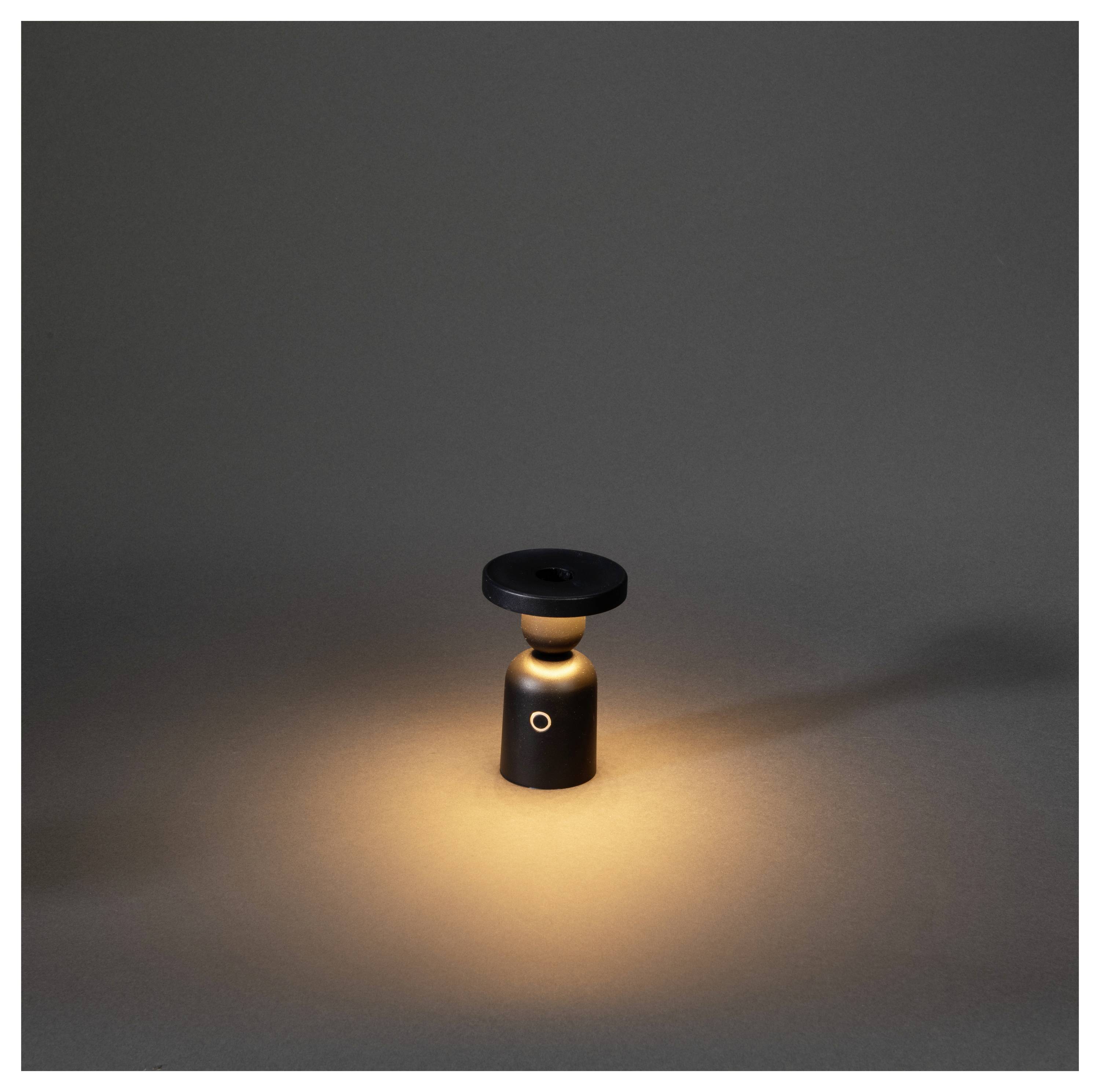Eine kleine, moderne schwarze Lampe strahlt einen warmen Glanz vor einem dunkelgrauen Hintergrund aus und erzeugt eine subtile, gemütliche Atmosphäre.