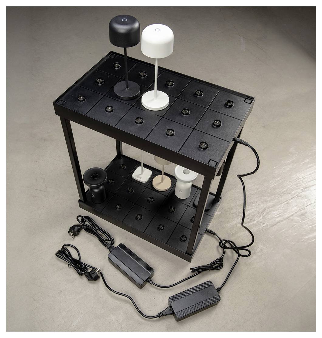 Ein schwarzes Regal trägt drei Paare kleiner zylindrischer Lampen, wobei jedes Paar eine andere Farbe hat: schwarz, weiß und beige. Zwei Netzadapter liegen auf dem Boden.