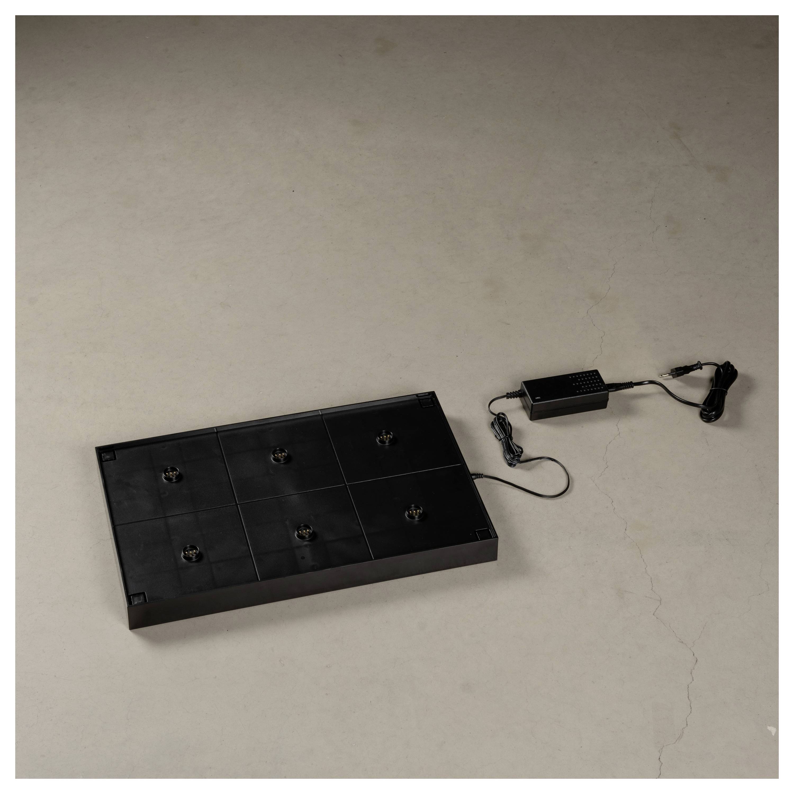Ein schwarzes rechteckiges elektronisches Gerät auf einer flachen Oberfläche, das über ein Kabel mit einem Netzteil verbunden ist.