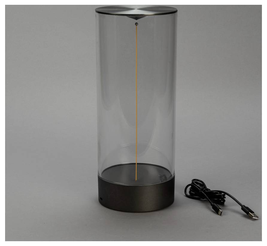 Ein zylindrischer transparenter Lautsprecher mit schwarzer Basis und sichtbarem vertikalem Draht im Inneren, versehen mit einem USB-Kabel an der Seite.