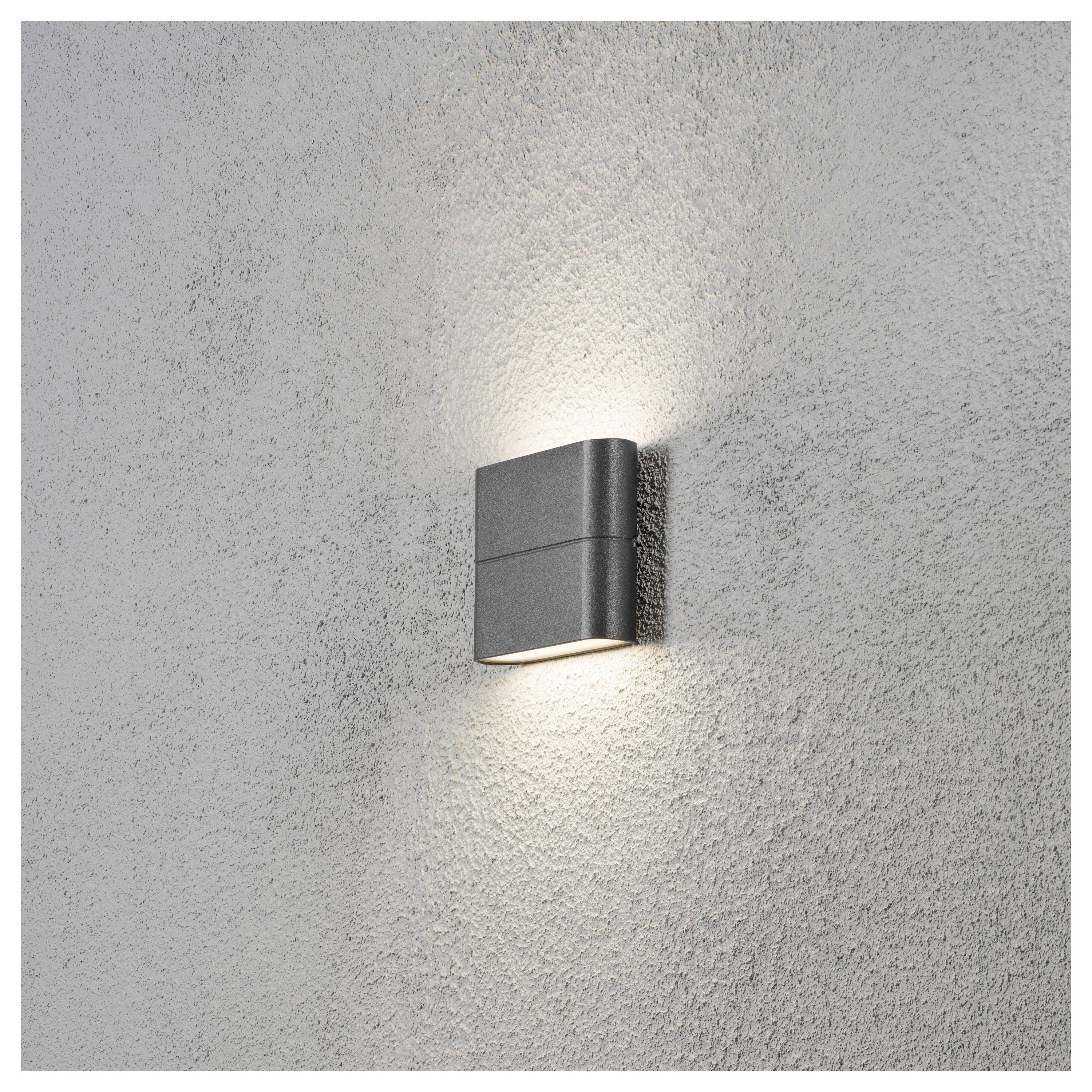Eine moderne Wandleuchte strahlt ein sanftes Licht vor einer strukturierten grauen Wand aus.