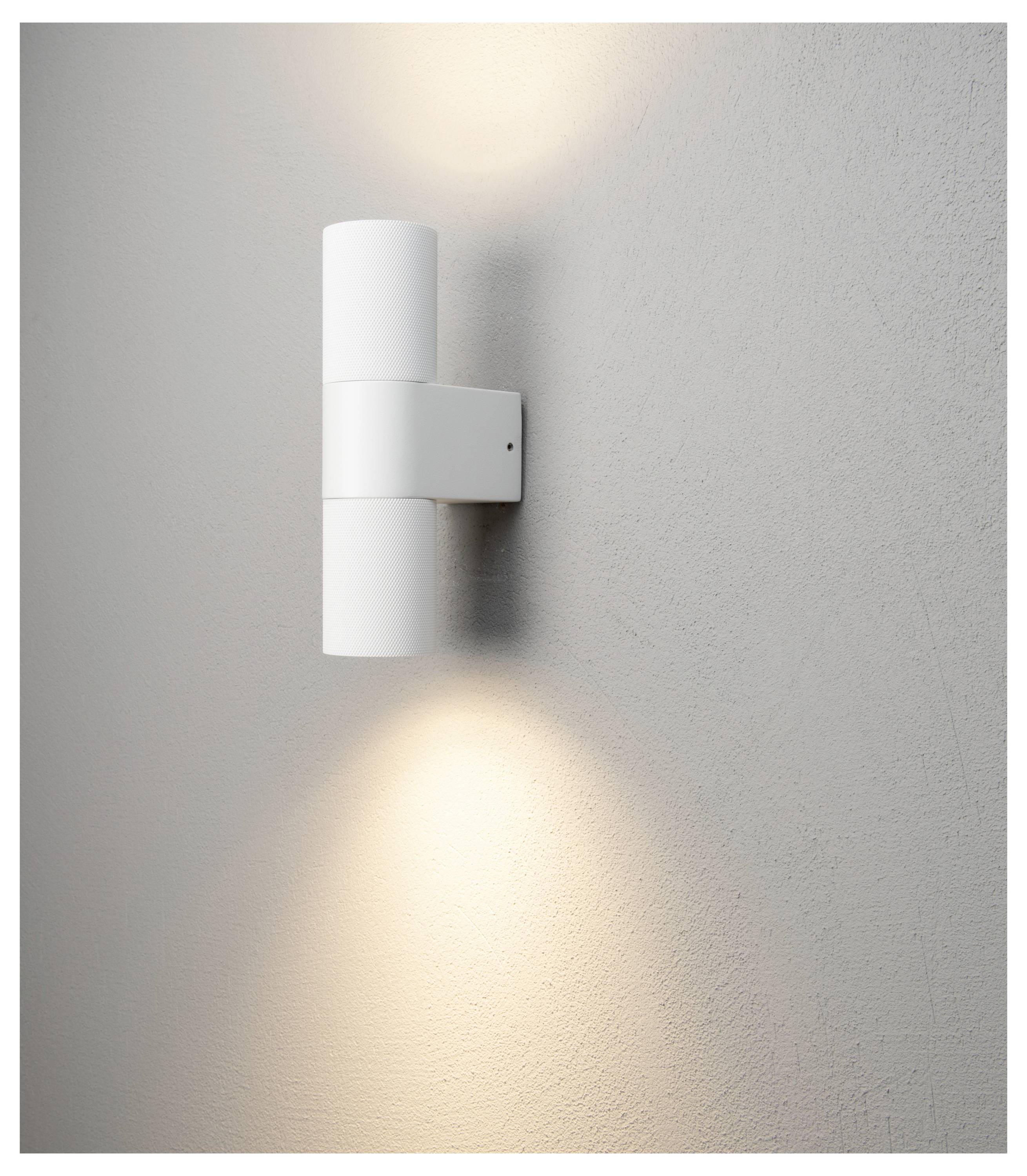 Eine moderne zylindrische weiße Wandlampe strahlt Licht nach oben und unten gegen eine strukturierte graue Wand und erzeugt eine sanfte Atmosphäre.
