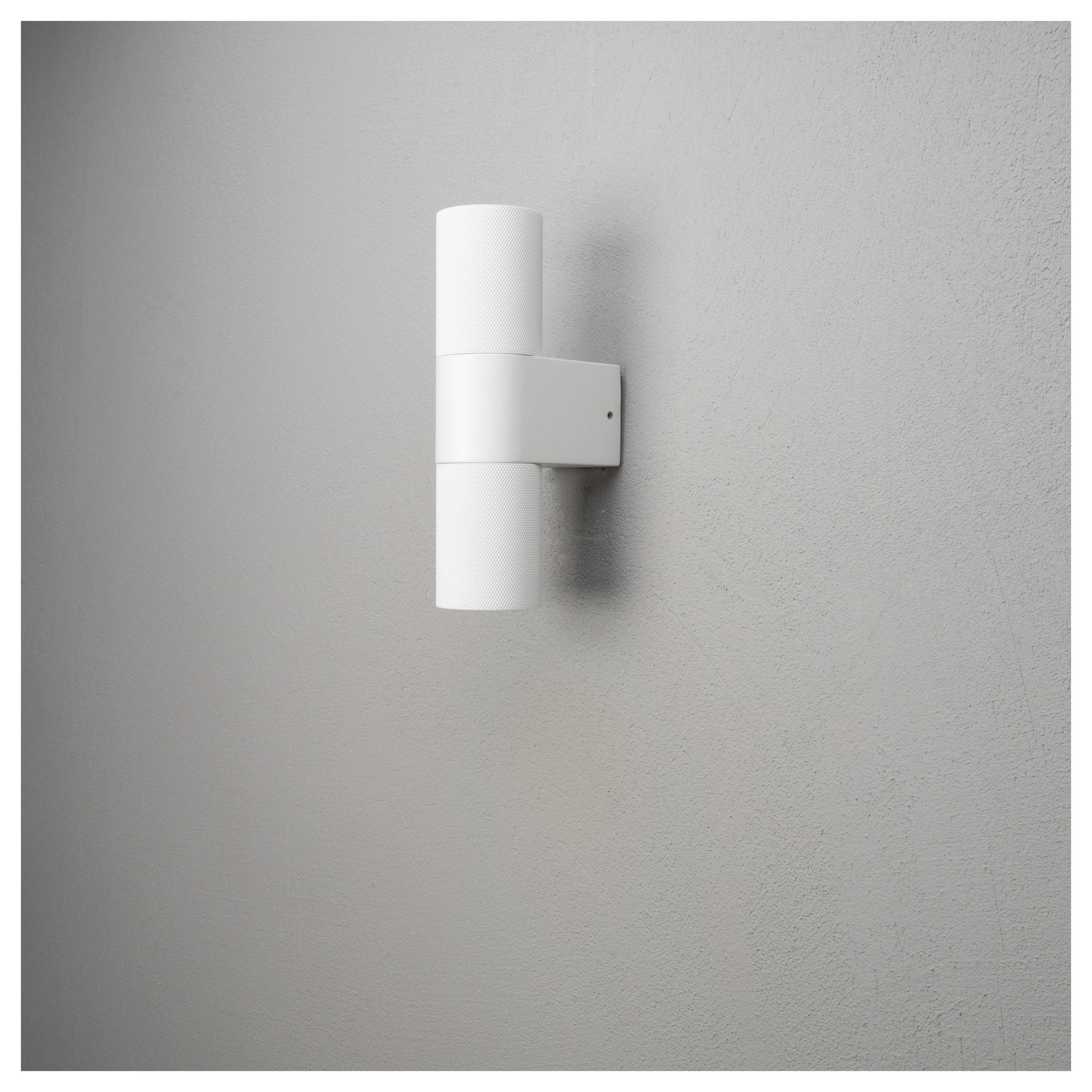 Eine weiße, zylindrische moderne Wandlampe ist an einer grauen Wand montiert, die Licht sowohl nach oben als auch nach unten wirft und dabei eine minimalistische Ästhetik erzeugt.