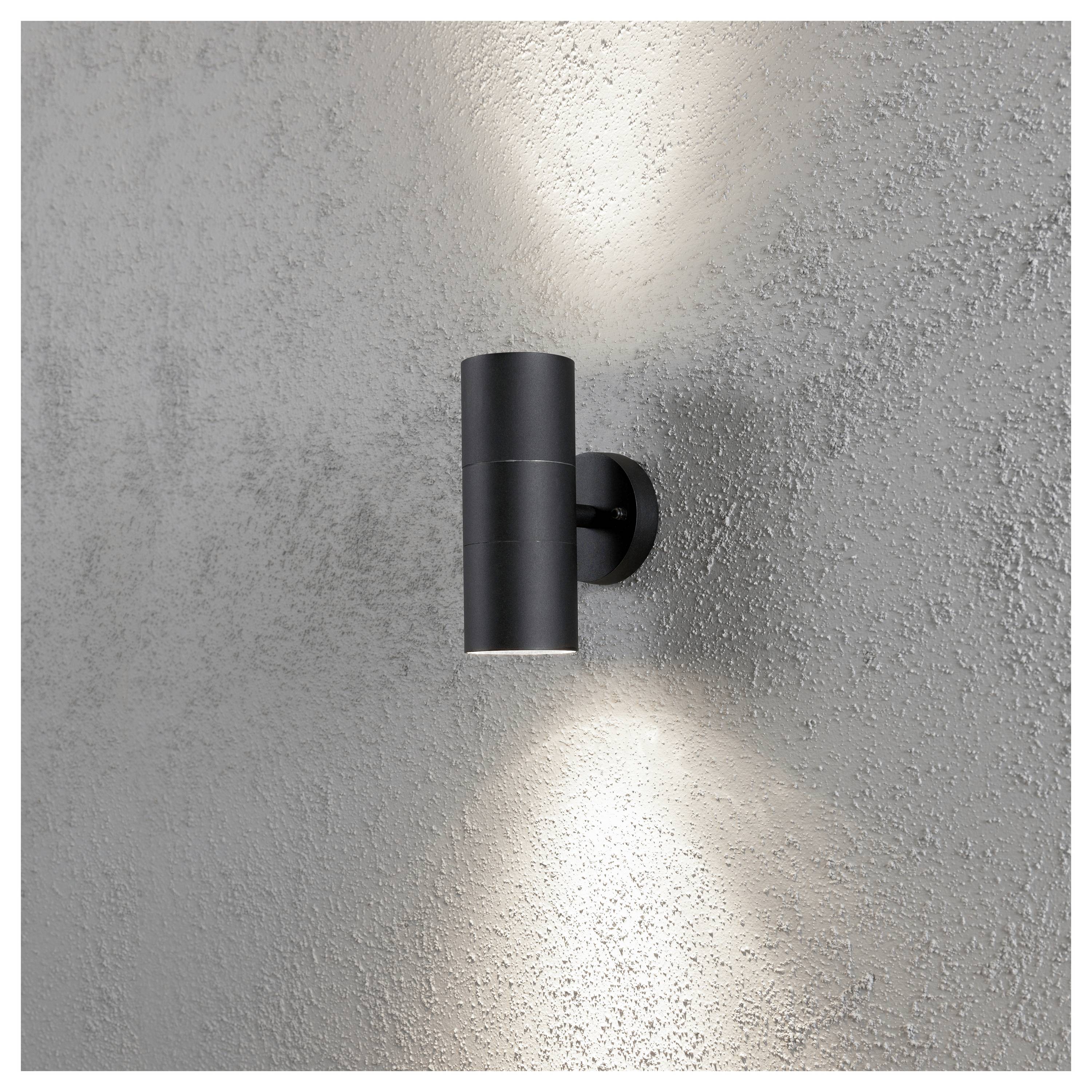Eine moderne schwarze Wandleuchte strahlt Licht nach oben und unten vor einer strukturierten grauen Wand aus und erzeugt einen eleganten Beleuchtungseffekt.