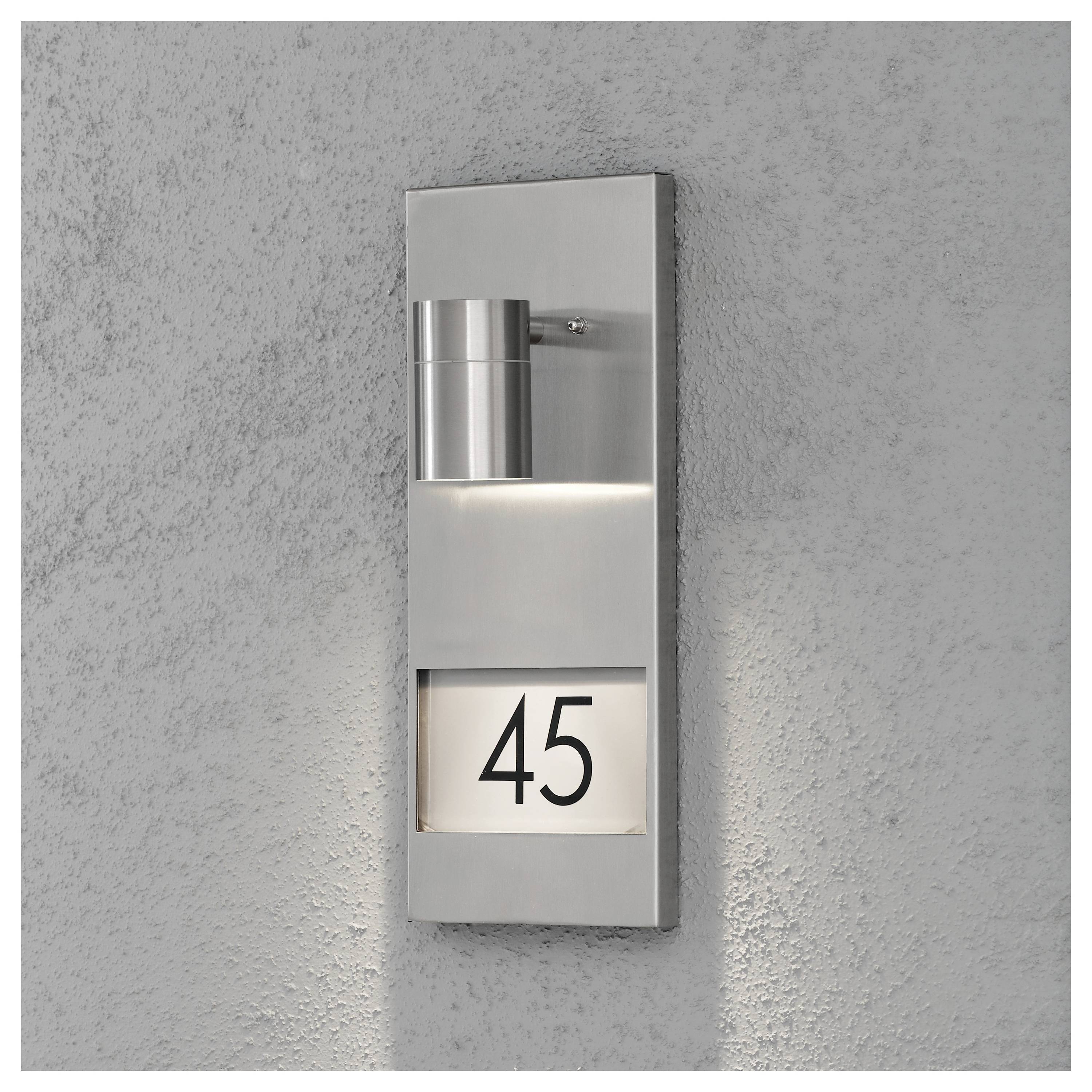 Eine moderne Außenwandleuchte mit Edelstahlfinish, die die Hausnummer '45' auf einer rechteckigen Plakette beleuchtet, die an einer Betonwand montiert ist.