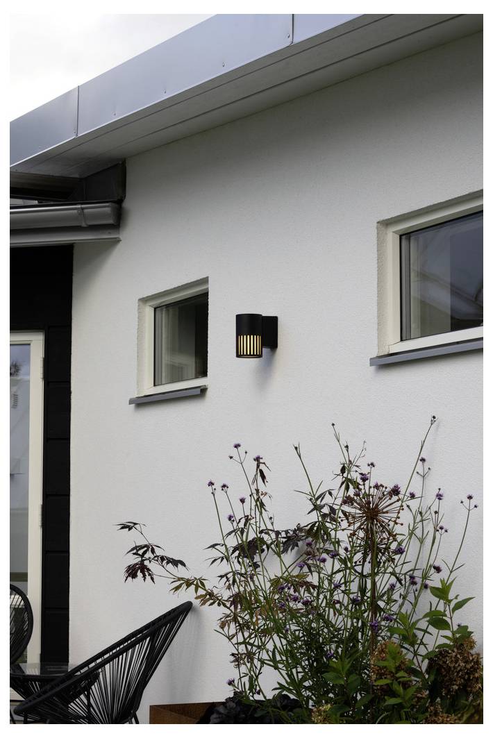 Eine moderne Außenleuchte an einer weißen Hauswand, umgeben von kleinen Fenstern und Vegetation.